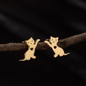 Boucles d'oreilles chat dorées minimalistes avec cœur ajouré sur fond de bois texturé noir