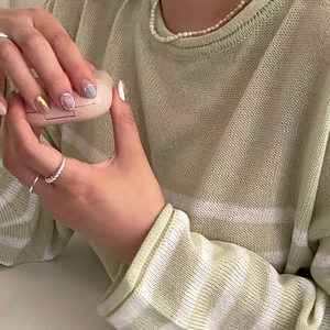 Detail of twisted silver knot ring and pearl necklace on a green knit sweater model