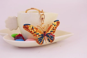 Close-up of a golden butterfly keychain with colorful crystals on a white teacup