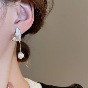 Close-up of elegant gold butterfly drop earrings with white pearls worn by a model