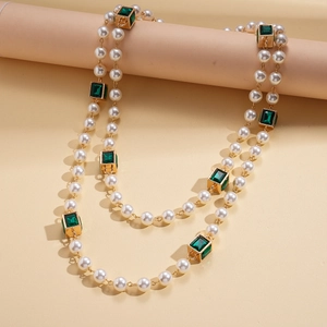Close-up of double-layer faux pearl necklace with green square gems and gold links