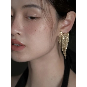 Close-up of golden long tassel earrings with delicate chains on a female model