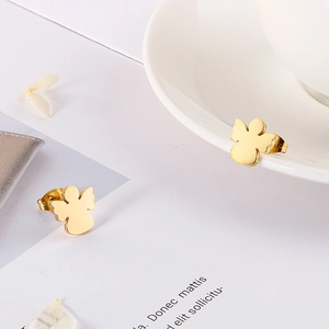 Close-up of golden angel earrings resting on a white ceramic cup with dried flowers