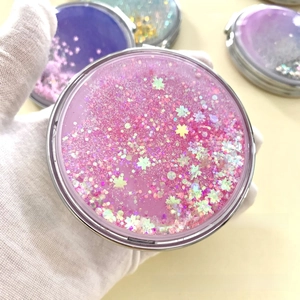Close-up of pink liquid glitter makeup mirror with star sequins and metal folding frame