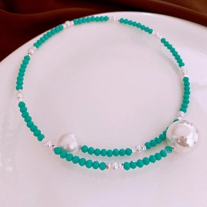 Detail of green beaded necklace with large silver spheres and pearls on a white plate