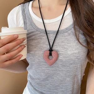 Pink heart-shaped pendant necklace with black cord on model with coffee cup