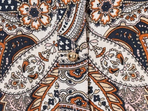 Gros plan sur un tissu à motif cachemire avec un bouton rond en métal doré poli