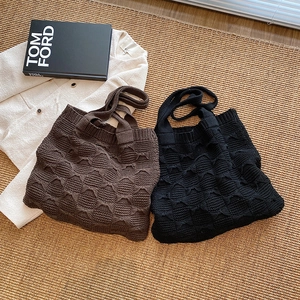 Flat lay of knit tote bags with 3D bow texture in brown and black on a woven rug