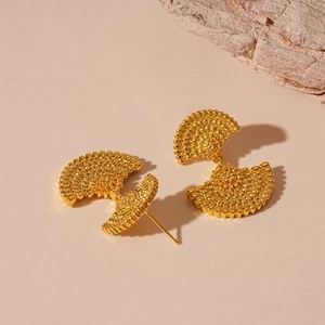 Detailed close-up of golden fan-shaped earrings with intricate granular metal texture