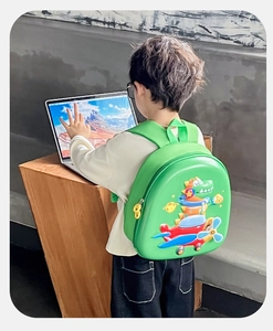 Vue latérale d'un sac à dos rigide dinosaure 3D vert porté par un enfant dans une pièce