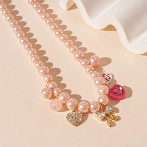 Détail du collier de perles roses avec pendentifs cœur et nœud sur support blanc