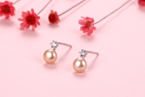 Macro view of freshwater pearl earrings with zircon inlay on a soft pink background