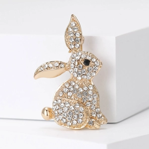 Sparkling golden rabbit brooch with clear rhinestones and black gem eye on white pedestal
