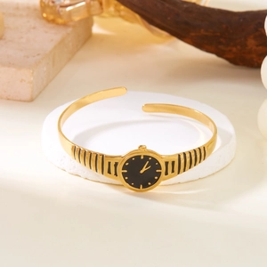 Detail of gold watch-style open cuff bracelet with black dial on a minimalist pedestal