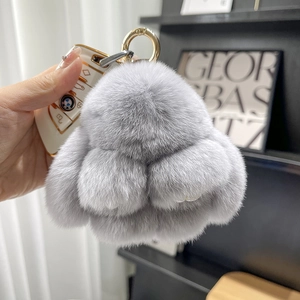 Close-up of a fluffy grey plush rabbit keychain with a gold ring held in hand