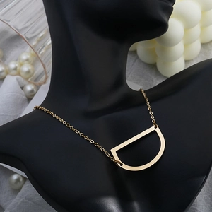 Elegant gold D-letter pendant necklace shown on a black model bust with pearl accents