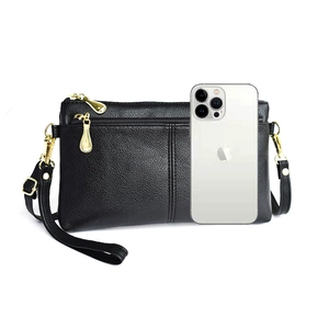 Detail of black pebbled leather crossbody bag with gold zippers next to a mobile phone