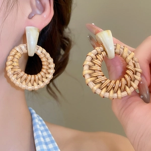 Detail of round woven rattan drop earrings with beige acrylic stud on a model