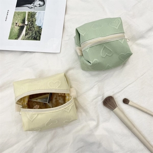 Détail de trousses à maquillage avec gaufrage cœur en vert menthe et beige avec zip