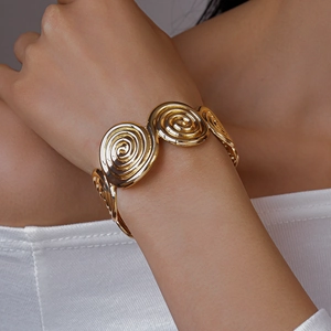 Macro detail of golden spiral disc metal cuff bracelet showing intricate textured geometric patterns