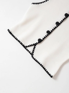 Makro-Detail der weißen Strickweste mit schwarzem Wellensaum und schwarzen Zierknöpfen