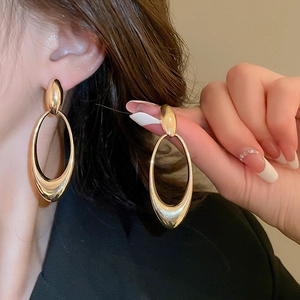 Close-up of a model wearing large polished gold oval hollow earrings with a metallic finish