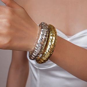 Detailed view of bold irregular textured wave bangles in gold and silver finish