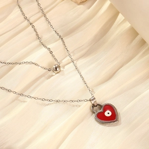 Detail of double-layer silver chain with red heart pendant and evil eye motif