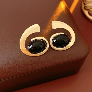 Détail de boucles d'oreilles spirales dorées avec pierre noire sur boîte en cuir