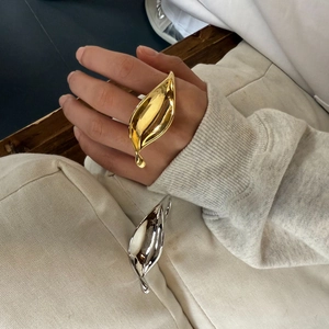 Detail shot of chunky gold and silver leaf rings styled on a model and textured fabric
