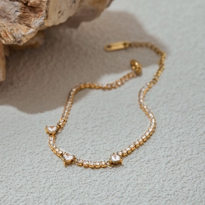 Macro detail of gold heart bracelet with sparkling white stones on a stone background