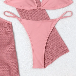 Detailed flat lay of pink three-piece bikini set with hollow knit cover-up on plush surface