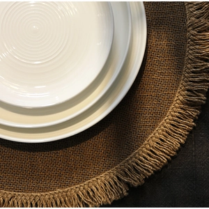 Round jute placemat with fringe edges and stacked textured white ceramic plates