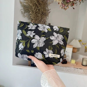 Detail of floral jacquard cosmetic bag in black with white flower patterns and logo label