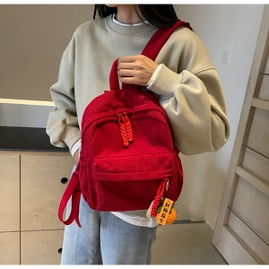 Red corduroy backpack detail featuring a zipper pocket and a cute crochet persimmon charm