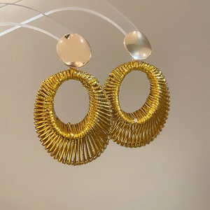 Détail de boucles d'oreilles ovales tissées dorées avec texture métallique sur fond