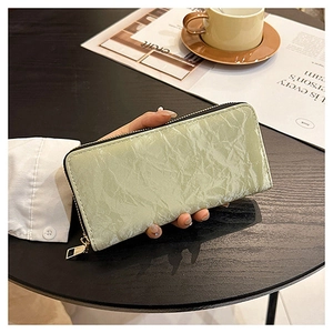 Lifestyle shot of mint green pleated long wallet held by hand next to a coffee cup