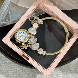 Detail of golden charm bracelet watch with flower pendants in a pink display box