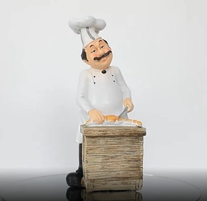 Chef figurine table decor with white hat and uniform slicing bread on wooden counter