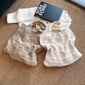 Flat lay of khaki and cream knitted tote bags with cable textures on a textured rug