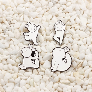 Detail of four white rabbit enamel pins showing different yoga and stretching poses