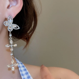 Macro shot of silver-toned rhinestone butterfly tassel earrings worn by a model