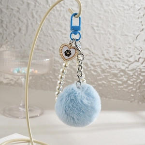 Détail du porte-clés pompon bleu avec chaîne en perles et pendentif coeur à motif floral