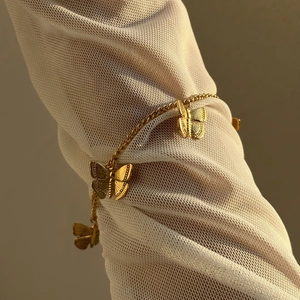 Vintage gold butterfly charm bracelet set against a white mesh sleeve background