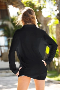 Back view of a breezy black long-sleeved beach cover-up shirt in a tropical garden setting