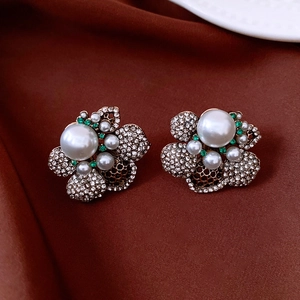 Close-up of French vintage flower stud earrings featuring pearls and green crystals.
