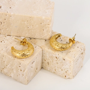 Close-up of gold semi-circle earrings with embossed heart pattern on stone