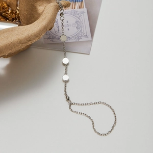 Detailed view of silver stainless steel chain bracelet with circular charms on paper bag