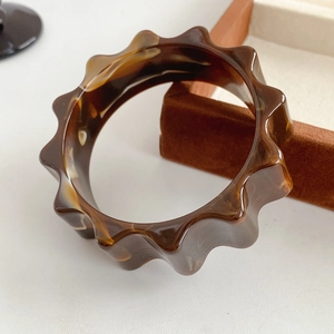 Macro view of wave-edge resin bangle with brown tortoiseshell texture on velvet box