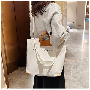 White canvas tote bag with brown leather handles and adjustable shoulder strap worn by model